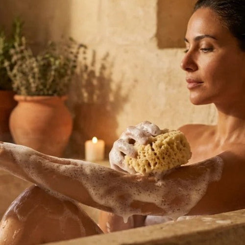 model in bath with natural sea sponge and lather on arm
